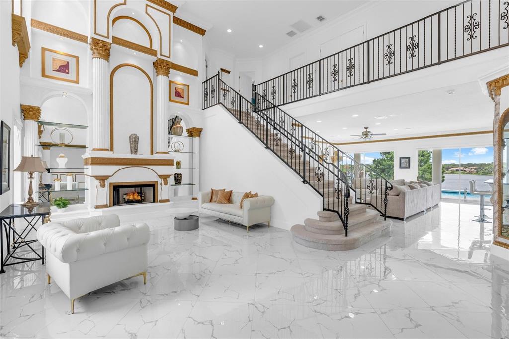 A grand living room features a fireplace, a staircase with iron railings, and marble flooring — 9656 WEATHERSTONE COURT, WINDERMERE, FL