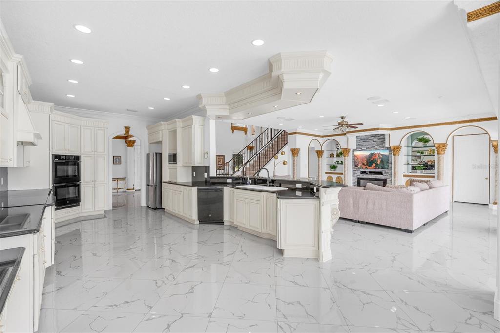 A spacious kitchen with white cabinetry, black countertops, and marble flooring overlooks a living area — 9656 WEATHERSTONE COURT, WINDERMERE, FL