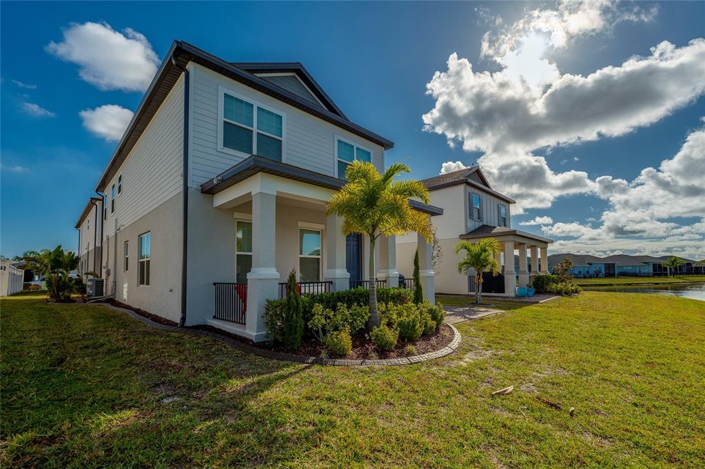 A two-story house with a front porch and palm tree sits beside a lake — 2912 MELETO BOULEVARD, NEW SMYRNA BEACH, FL