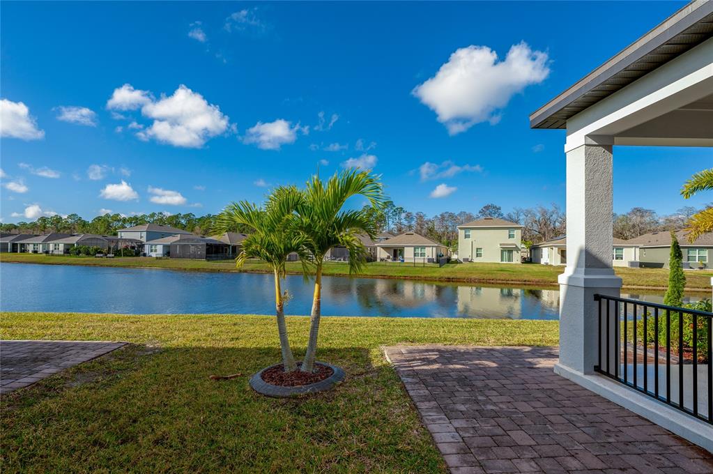 A view from a paved patio overlooking a lake and neighboring houses under a blue sky — 2912 MELETO BOULEVARD, NEW SMYRNA BEACH, FL
