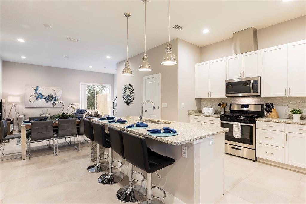 A modern kitchen with white cabinets, granite countertops, and a breakfast bar with black stools — 7546 SUNVILLE AVENUE, KISSIMMEE, FL