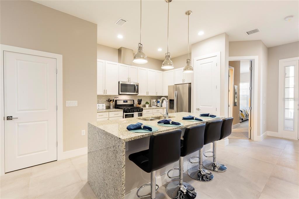A kitchen features white cabinets, granite countertops, a central island with bar stools, and stainless appliances — 7546 SUNVILLE AVENUE, KISSIMMEE, FL