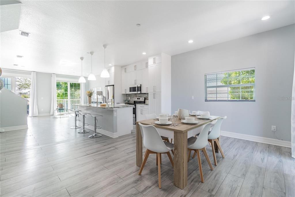 A bright, open-concept kitchen and dining area featuring white cabinetry, a breakfast bar, and wood-look flooring — 2108 1ST STREET, INDIAN ROCKS BEACH, FL