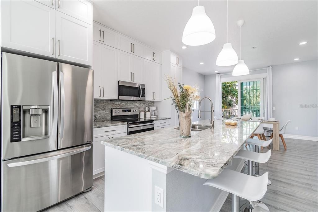 A modern kitchen features white cabinets, granite countertops, stainless steel appliances, and a breakfast bar — 2108 1ST STREET, INDIAN ROCKS BEACH, FL