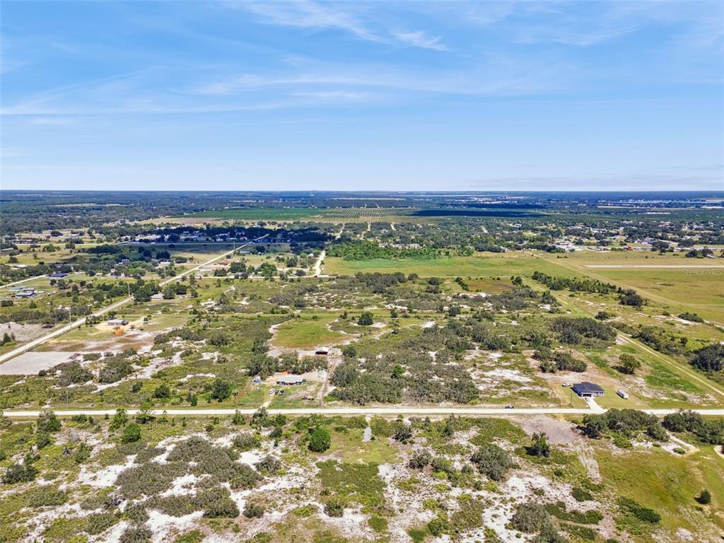 An aerial view shows a rural landscape with scattered trees, open fields, and a paved road — 2253 W SHULA ROAD, AVON PARK, FL