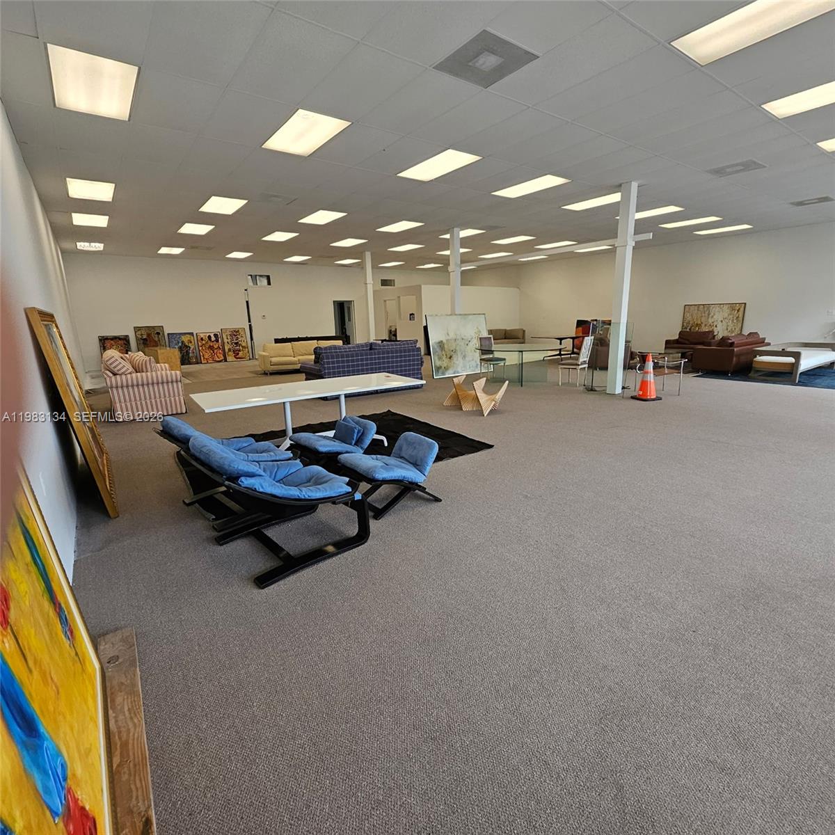 A large, open-plan commercial space features carpeted flooring, drop ceilings with recessed lighting, and scattered furniture — 2025 13th Ave, FL 32960, FL