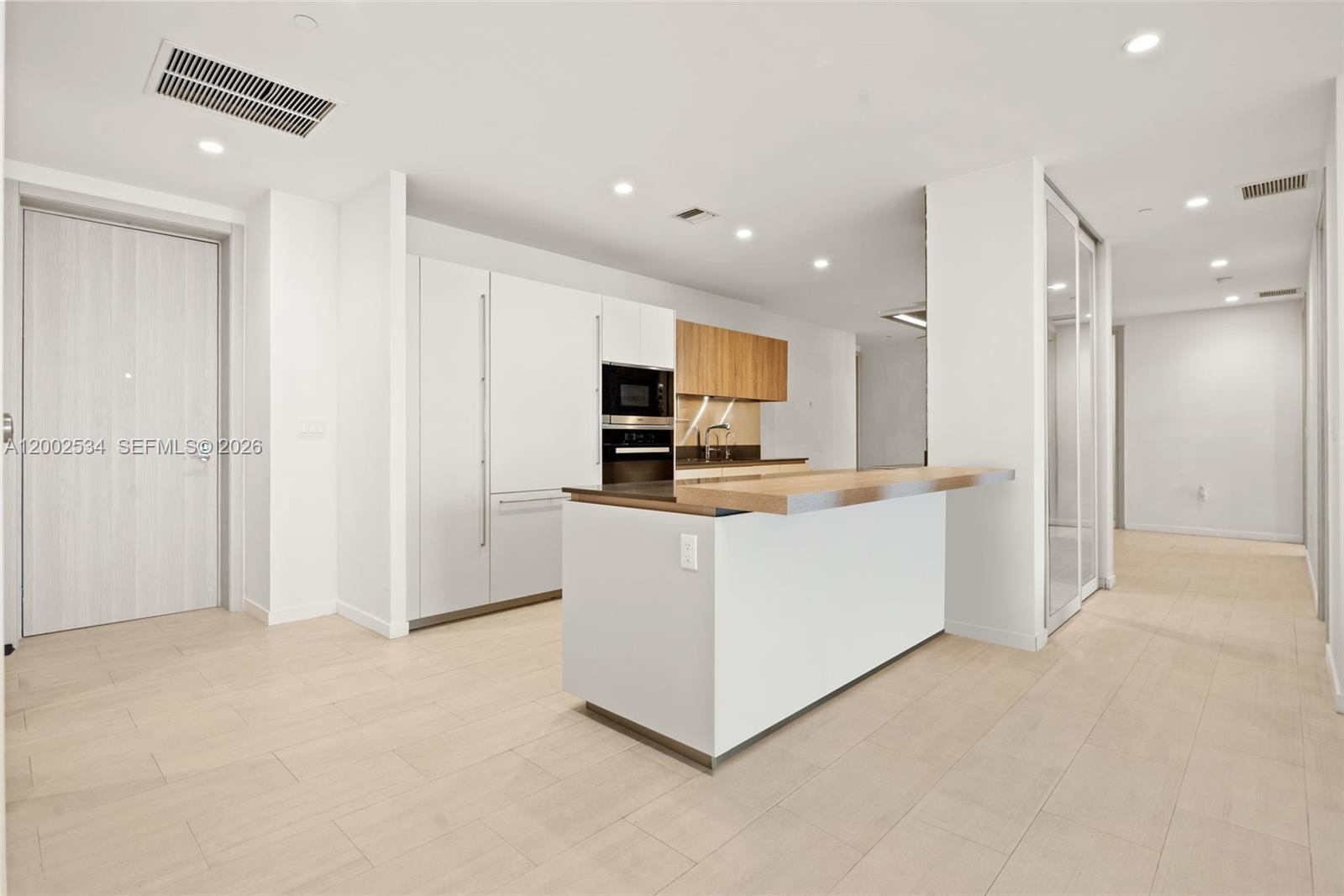 A modern kitchen features white cabinetry, a wooden breakfast bar, and light-colored tile flooring — 1000 Brickell Plz, Miami FL 33131, MIAMI, FL