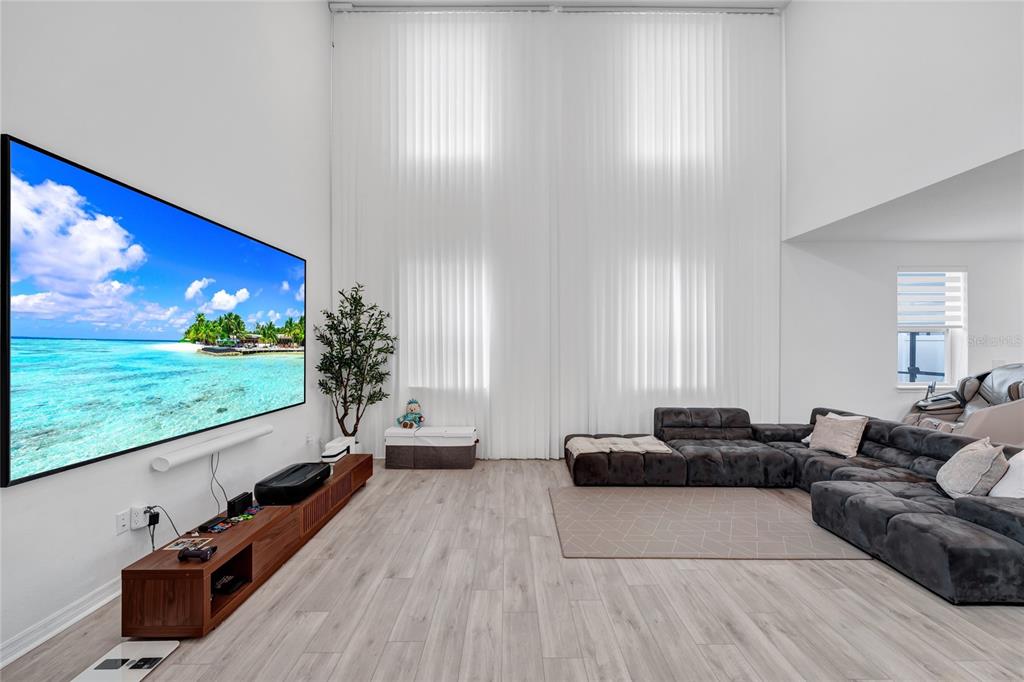 A spacious living room features a large wall-mounted television, a sectional sofa, and tall windows — 17018 SEVILLE ORANGE ROAD, WINTER GARDEN, FL