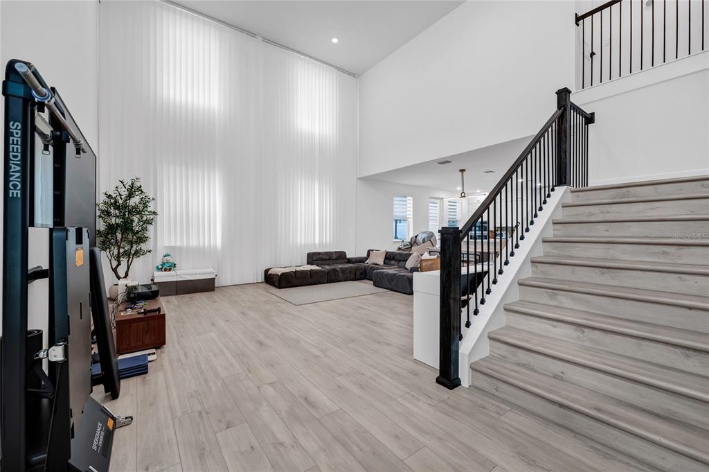 A living room with tall windows, light wood flooring, and a staircase with black railings — 17018 SEVILLE ORANGE ROAD, WINTER GARDEN, FL
