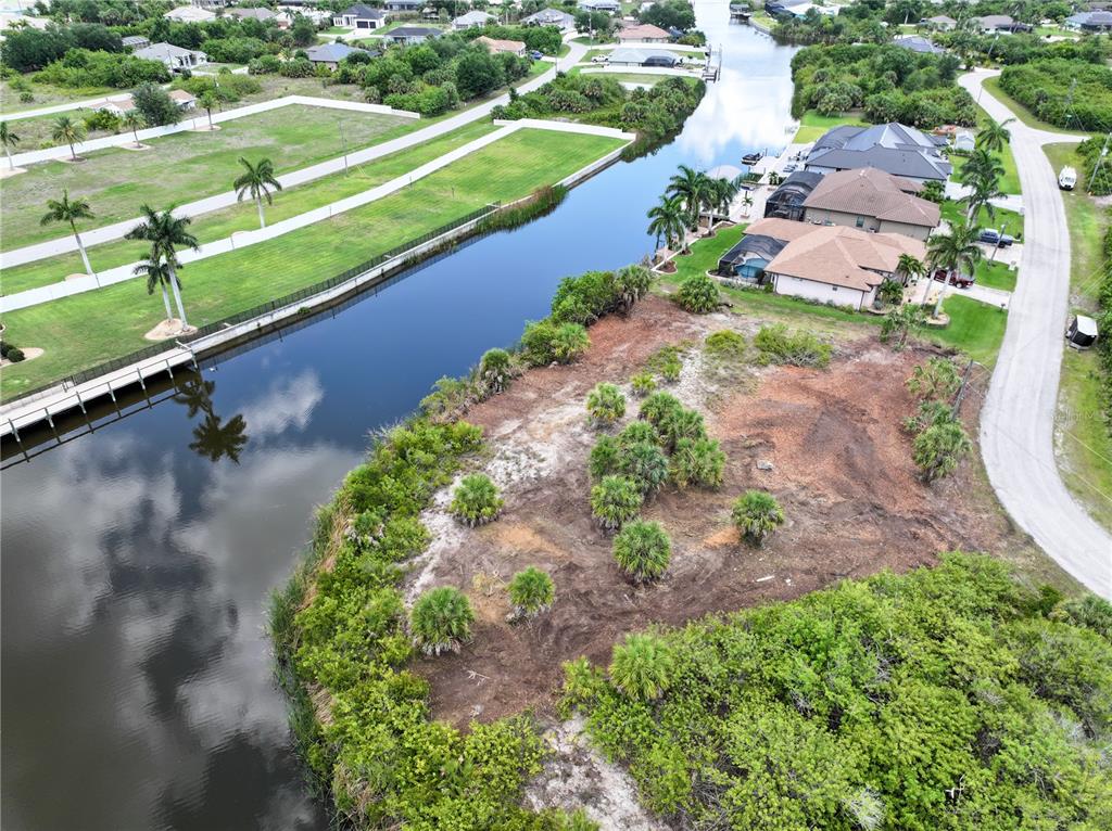 An aerial view shows a vacant waterfront lot with sparse vegetation next to residential houses — 14235 FRUITPORT CIRCLE, PORT CHARLOTTE, FL