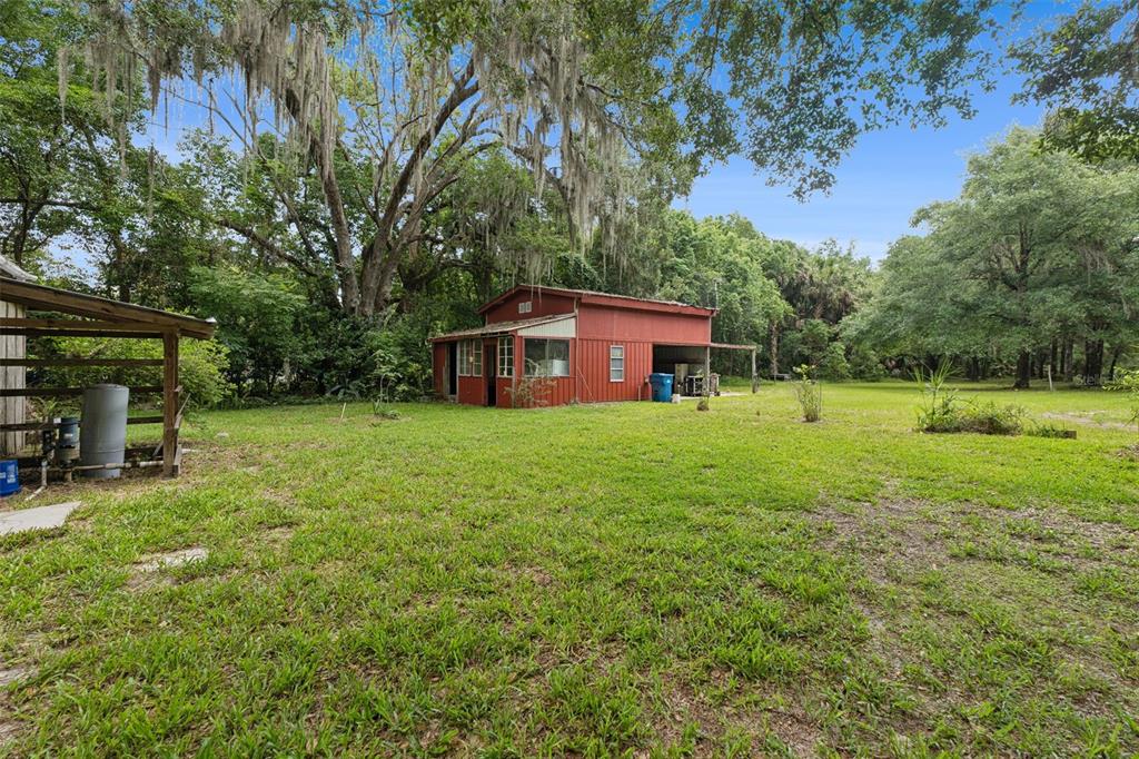 A red barn-style building sits in a grassy yard surrounded by large, moss-draped trees — 1555 CHURCH STREET, PIERSON, FL