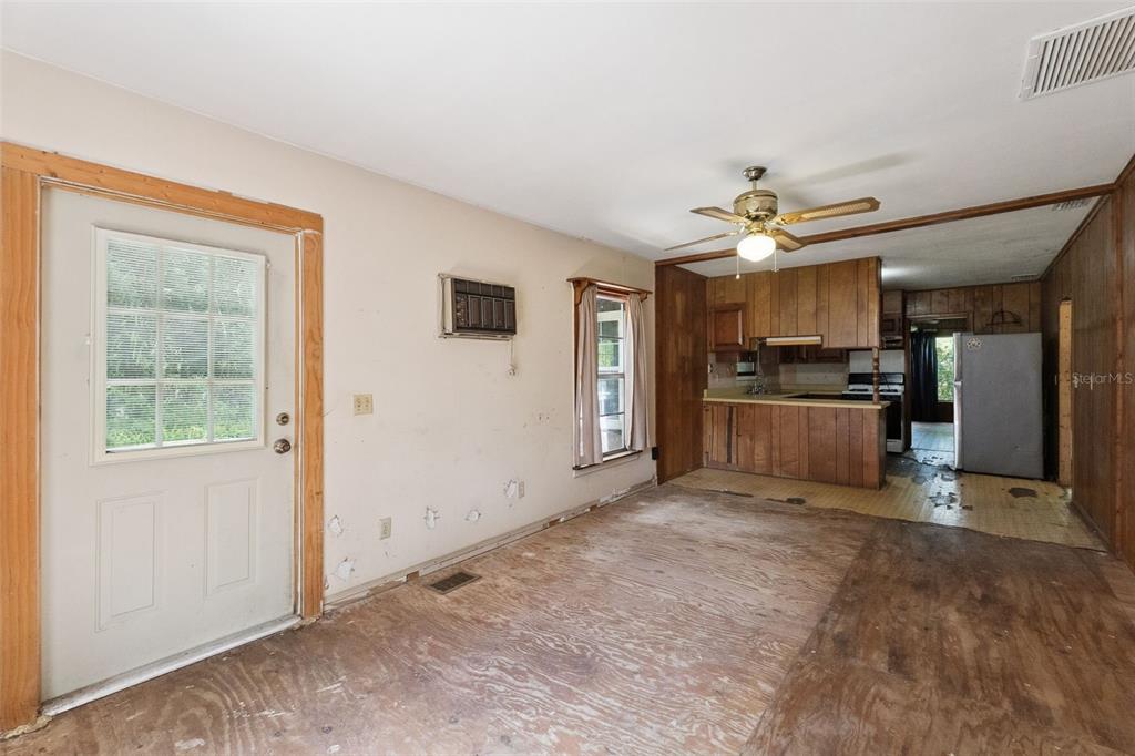An interior view shows a living area with exposed subflooring leading to a wood-paneled kitchen — 1555 CHURCH STREET, PIERSON, FL