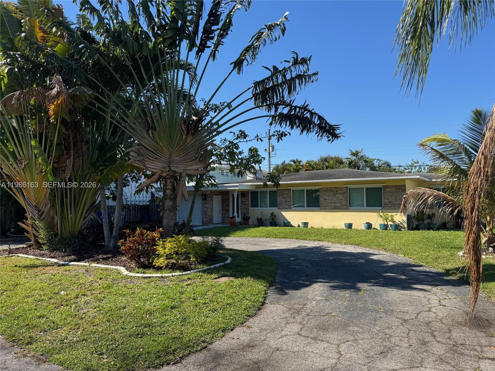 A single-story house with a stone facade and yellow paint features a curved driveway — 2355 SE 7th St, Pompano Beach FL 33062, POMPANO BEACH, FL