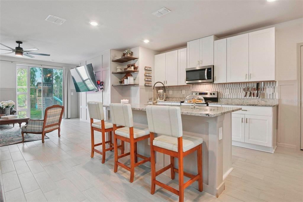A kitchen with white cabinets, granite countertops, and three bar stools faces a living area — 3610 RADIANT MOUNTAIN DRIVE, PLANT CITY, FL