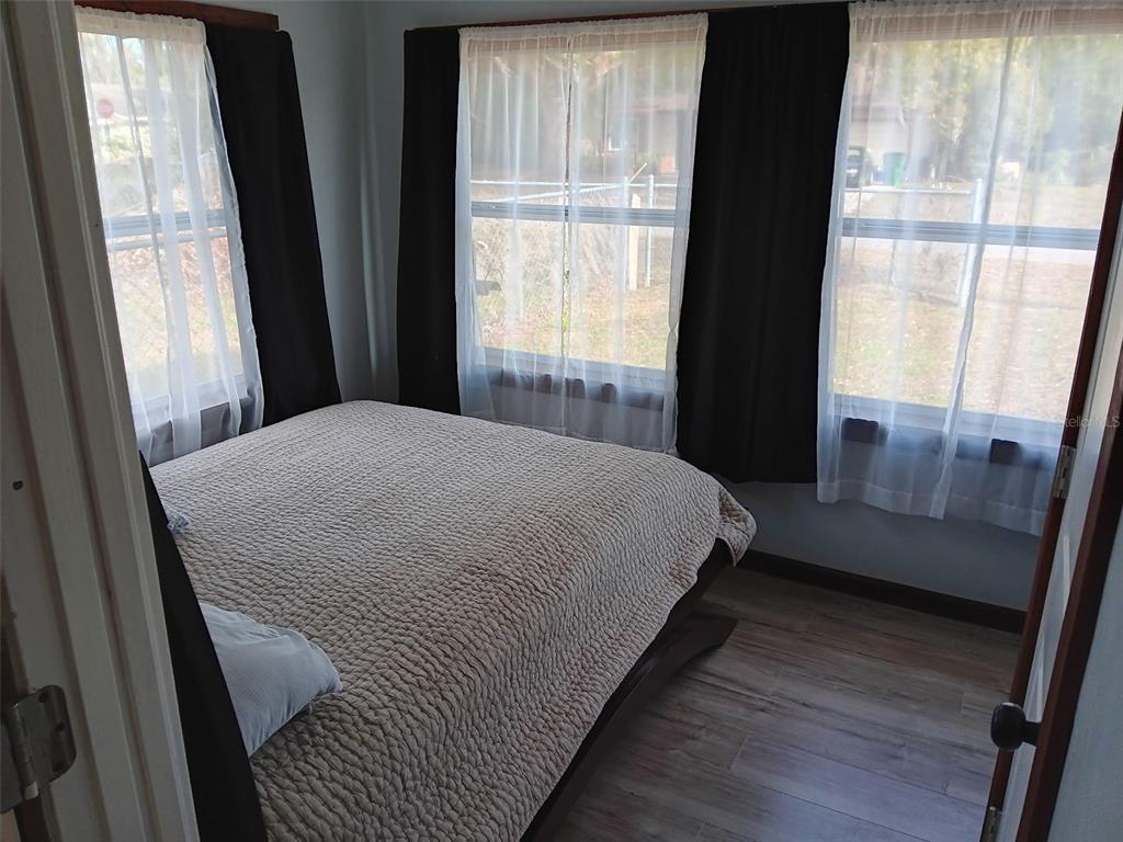 A bedroom features a bed with a textured quilt, wood-look flooring, and windows with curtains — 5647 19TH STREET, ZEPHYRHILLS, FL