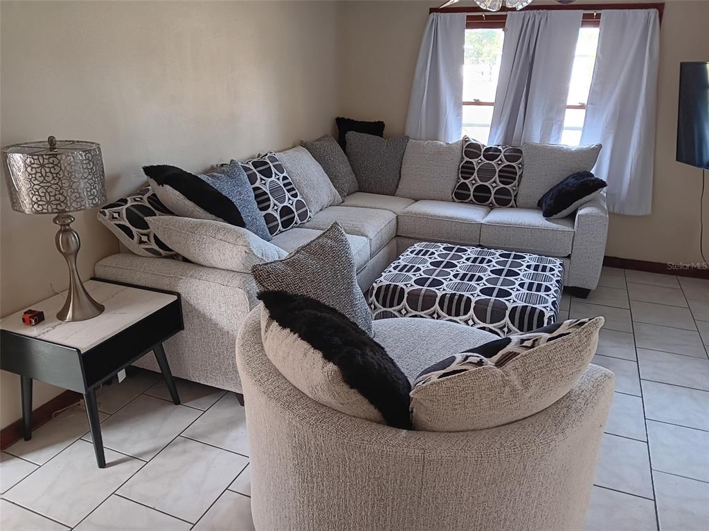 A living room features a large gray sectional sofa, a matching ottoman, and tiled flooring — 5647 19TH STREET, ZEPHYRHILLS, FL