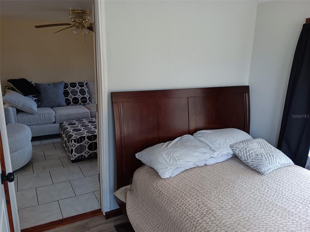 A bedroom with a dark wood headboard is visible through a doorway leading to a living room — 5647 19TH STREET, ZEPHYRHILLS, FL