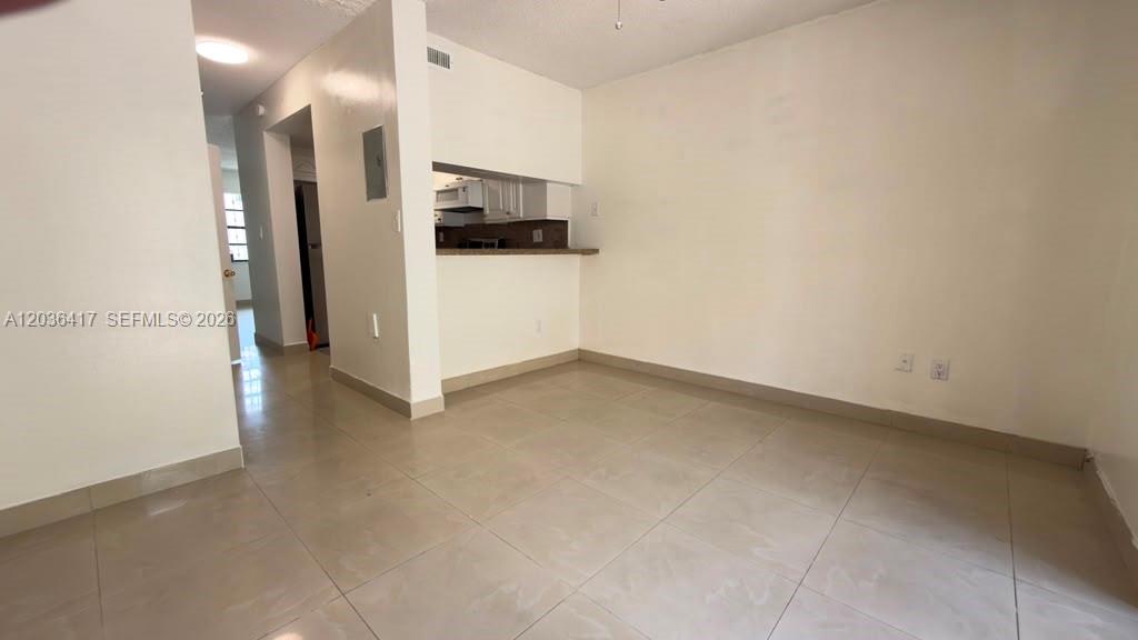 An empty room with light-colored tile flooring and a pass-through opening to a kitchen — 5388 W 24th Ave # 110, Hialeah FL 33016, HIALEAH, FL