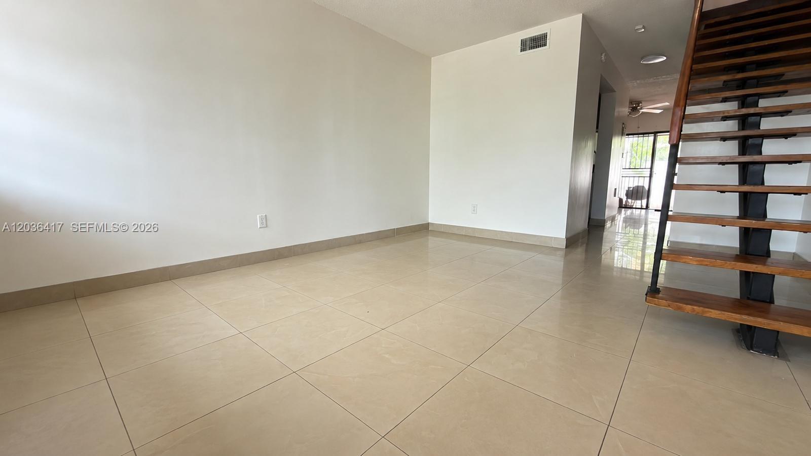 An empty room features light-colored tile flooring, white walls, and a wooden staircase — 5388 W 24th Ave # 110, Hialeah FL 33016, HIALEAH, FL