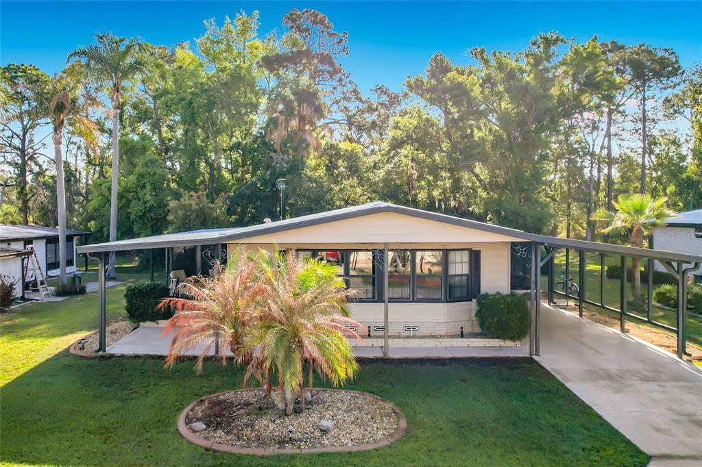 A single-story manufactured home with a covered carport and a front yard palm tree — 6561 CHINABERRY DR NE, WINTER HAVEN, FL