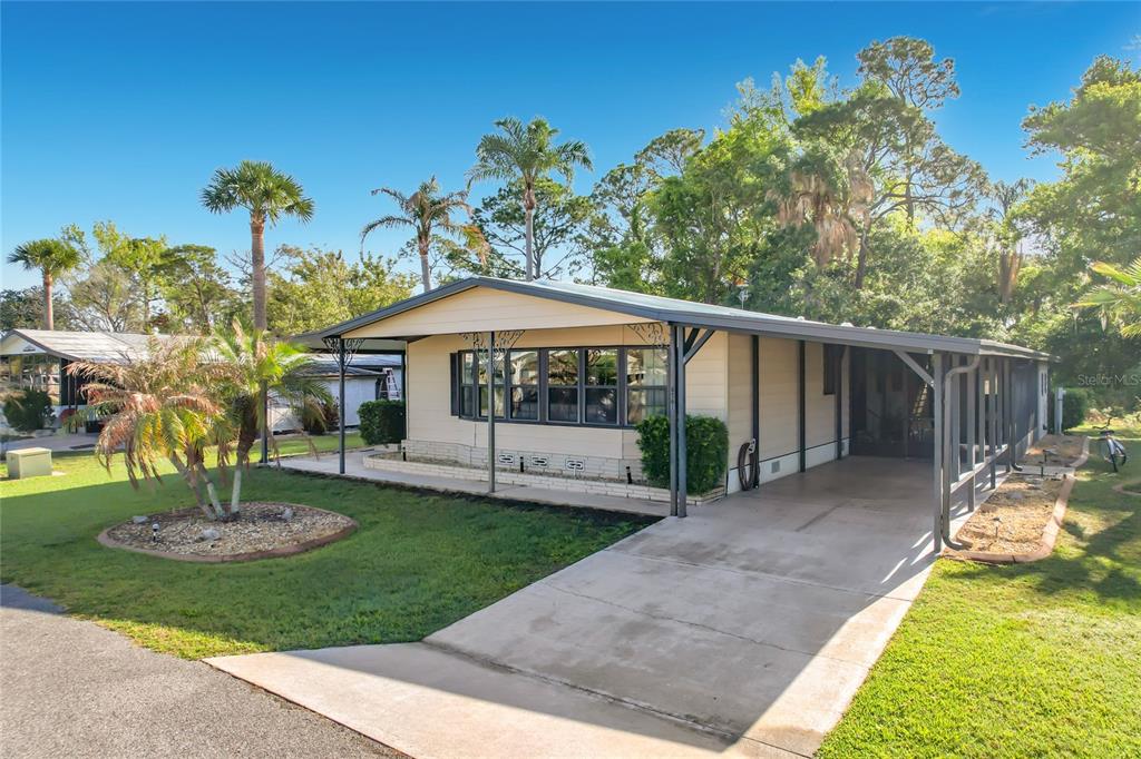 A single-story mobile home with a carport, tan siding, and a front lawn with palms — 6561 CHINABERRY DR NE, WINTER HAVEN, FL