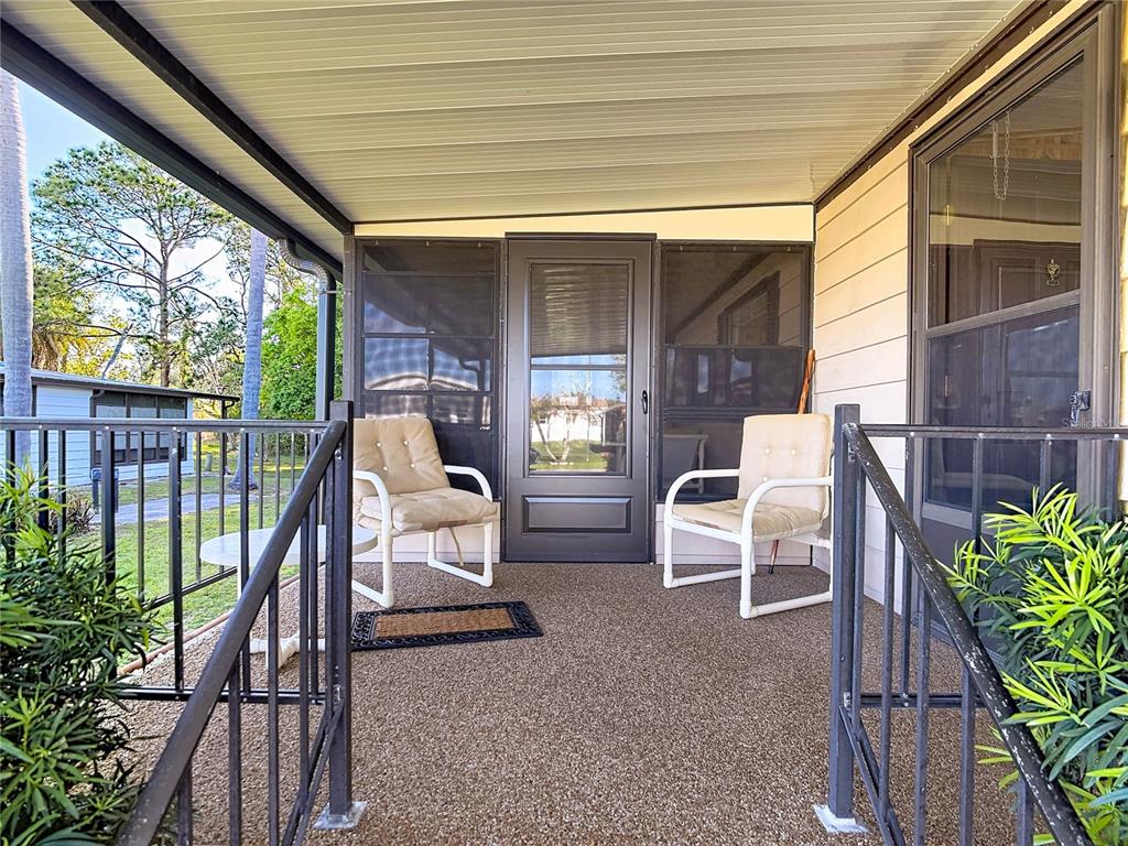 A covered porch features a textured floor, two chairs, and a screen door — 6561 CHINABERRY DR NE, WINTER HAVEN, FL