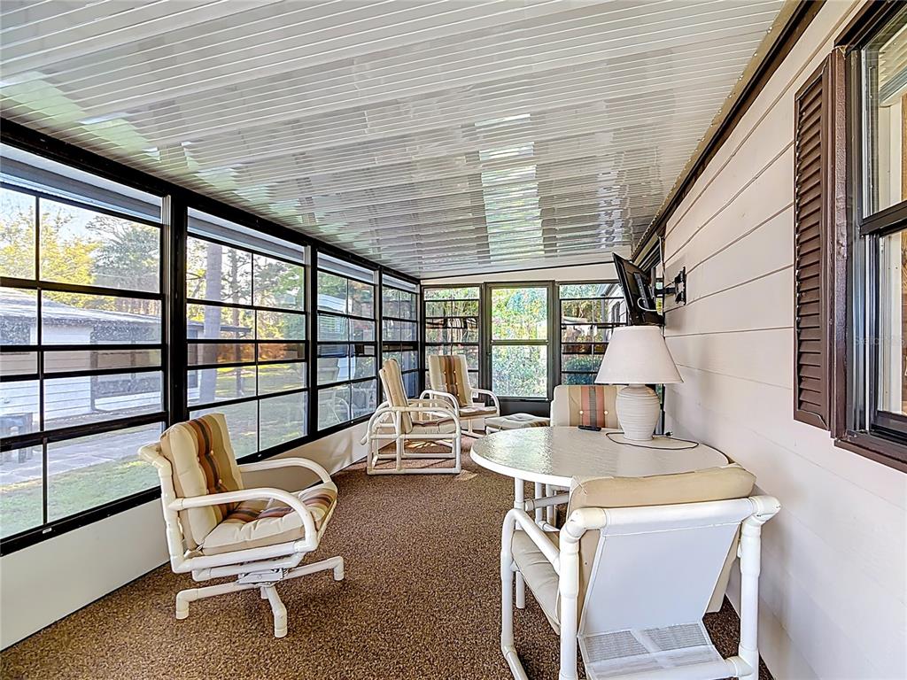 A sunroom features a table, chairs, carpeted flooring, and large windows overlooking a yard — 6561 CHINABERRY DR NE, WINTER HAVEN, FL