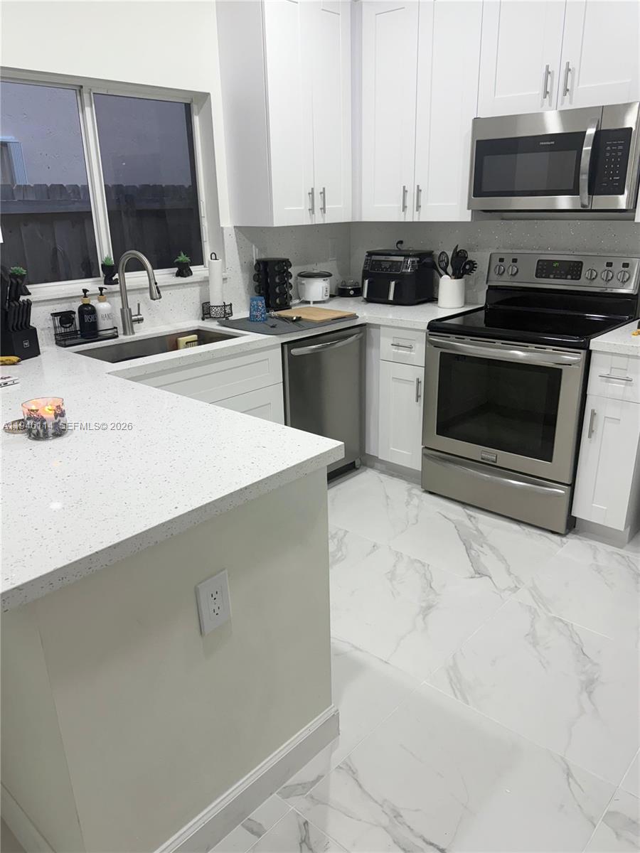 A modern kitchen features white cabinets, quartz countertops, stainless steel appliances, and marble-patterned tile flooring — 22844 SW 114th Ave, Miami FL 33170, MIAMI, FL