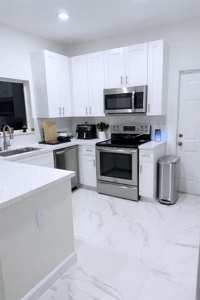 A modern kitchen features white cabinets, stainless steel appliances, and white marble-patterned tile flooring — 22844 SW 114th Ave, Miami FL 33170, MIAMI, FL