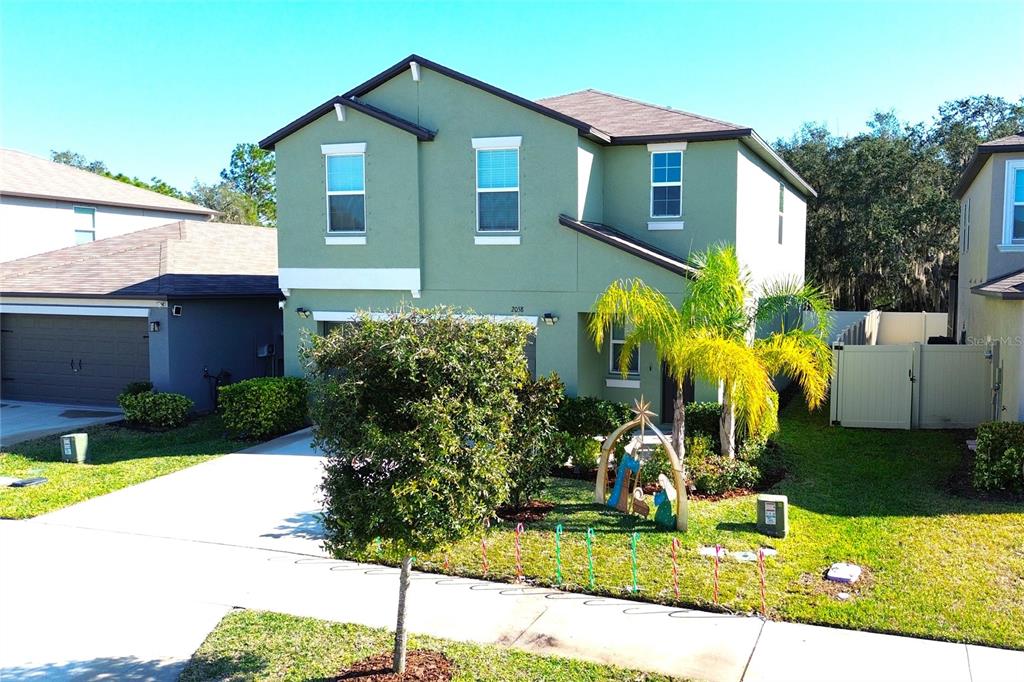 A two-story green house with a driveway, a front yard, and a small nativity display — 2058 STELLAR BRILLIANCE WAY, LUTZ, FL