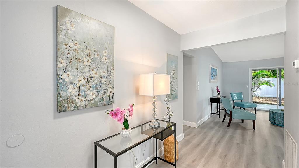 A bright entryway features a glass console table, floral artwork, and a view into a living area — 4054 PALAU DRIVE, SARASOTA, FL