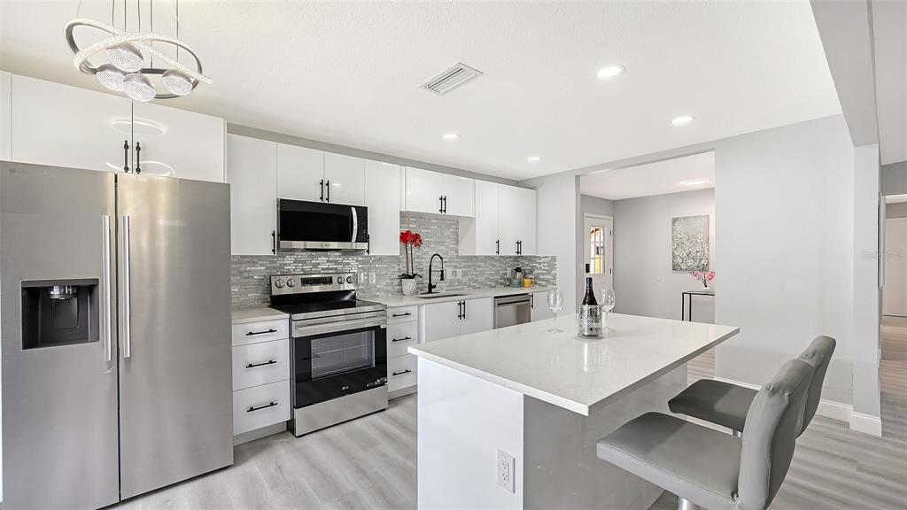 A modern kitchen features white cabinets, stainless steel appliances, a gray island, and light flooring — 4054 PALAU DRIVE, SARASOTA, FL