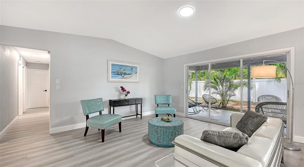 A living room with light gray flooring, two teal chairs, a round ottoman, and sliding doors — 4054 PALAU DRIVE, SARASOTA, FL