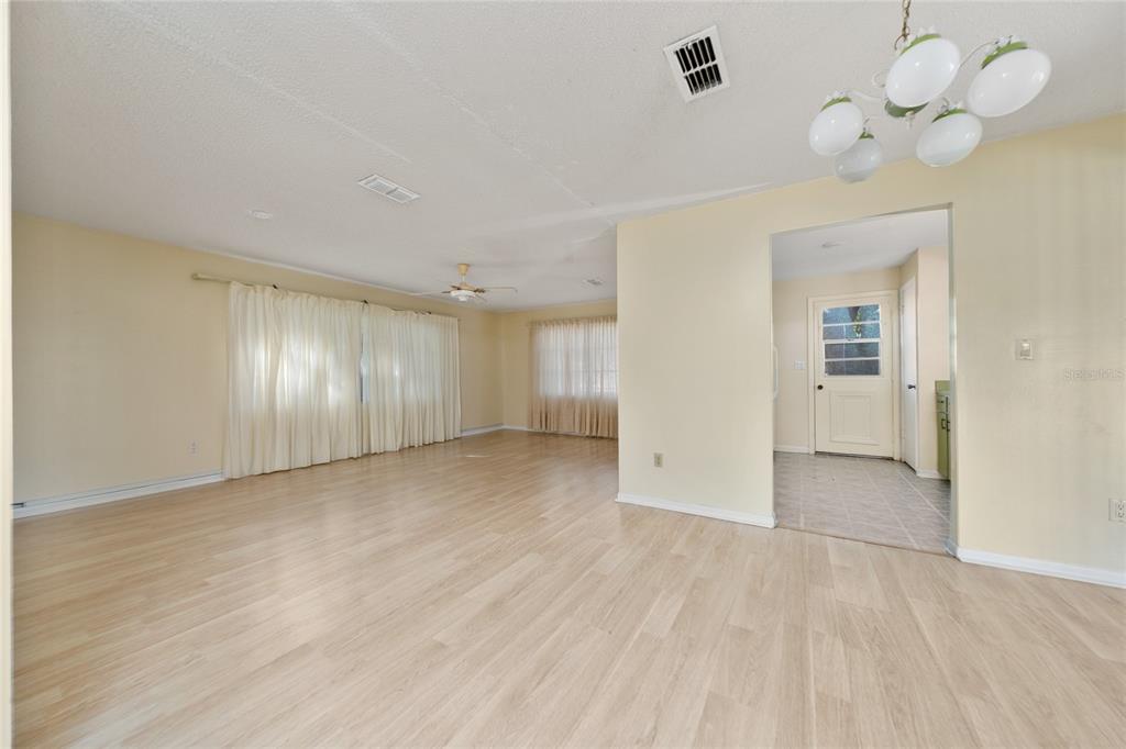 A spacious living room with light wood-look flooring, pale yellow walls, and white curtains — 14644 SW 35TH TERRACE ROAD, OCALA, FL