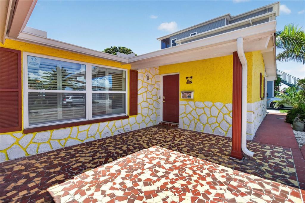 A yellow house exterior features a red door, stone-patterned walls, and a tiled patio — 12805 FIFTH ISLE, HUDSON, FL