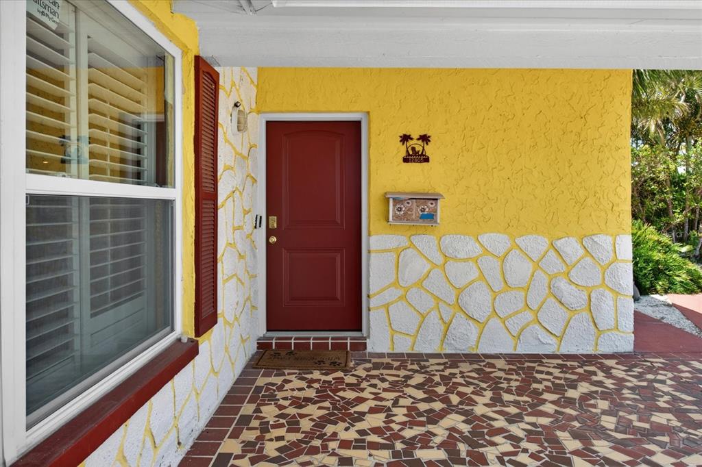 A bright yellow exterior wall with stone accents, a red front door, and a tiled porch — 12805 FIFTH ISLE, HUDSON, FL