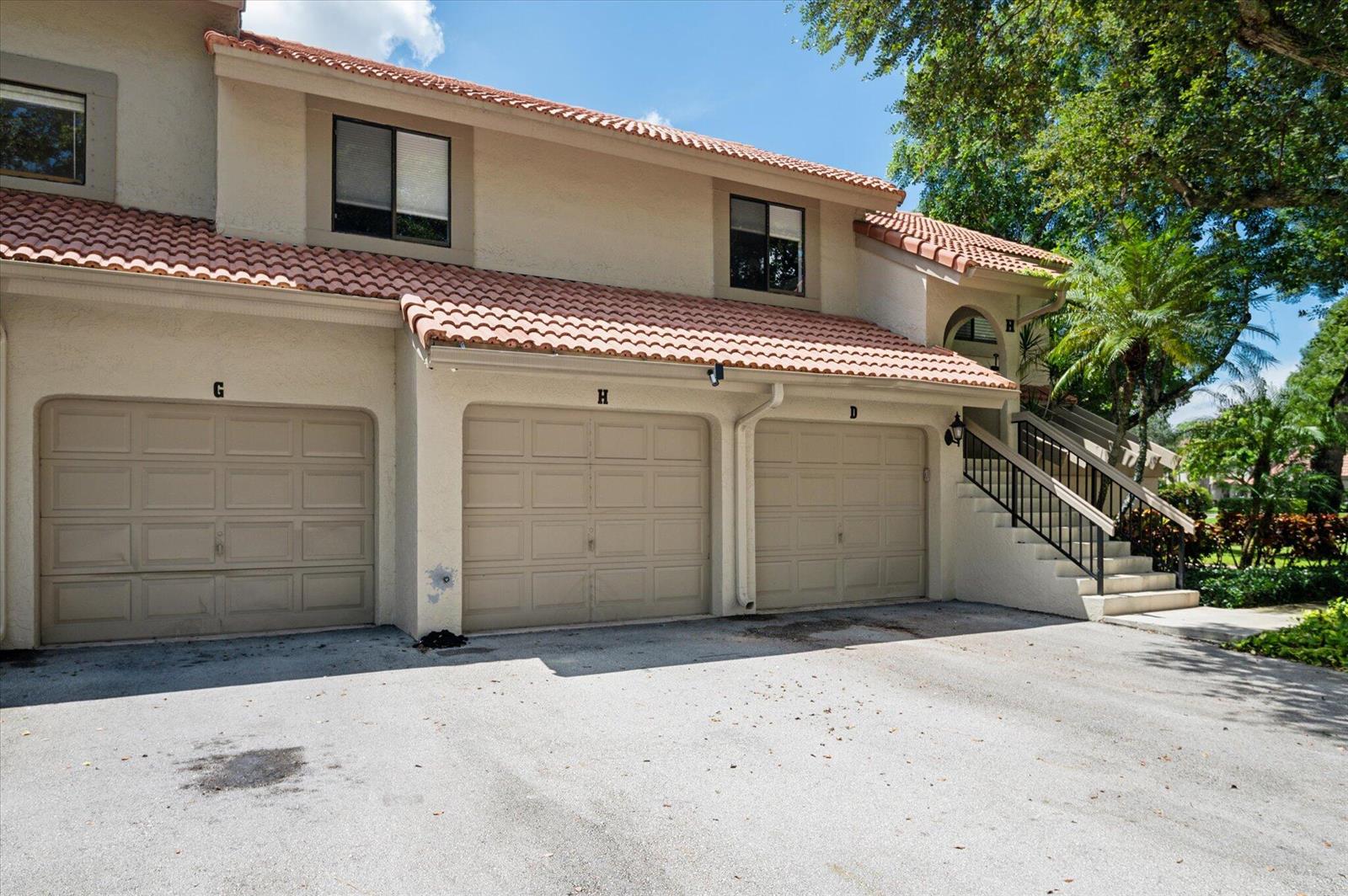 Exterior view of a multi-unit residential building with three garage doors and an outdoor staircase — 5750 Coach House Circle # G, Boca Raton FL 33486, BOCA RATON, FL