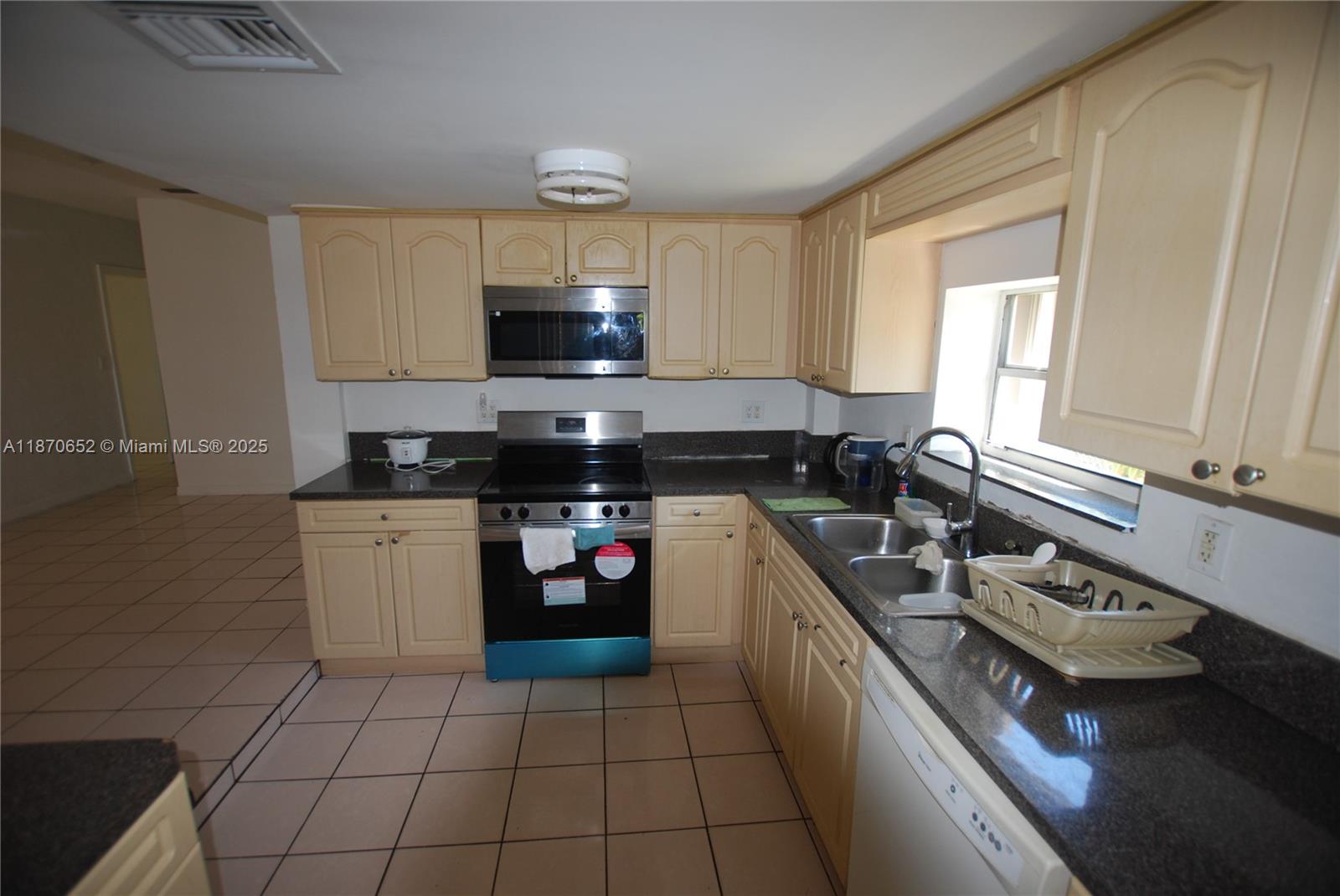 A kitchen features light wood cabinets, dark granite countertops, stainless steel appliances, and tiled flooring — 1801 NE 176th St, North Miami Beach FL 33162, NORTH MIAMI BEACH, FL