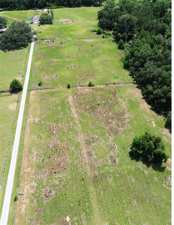 An aerial view shows a large, fenced grassy lot bordered by a road and trees — TBD W HWY 326, OCALA, FL