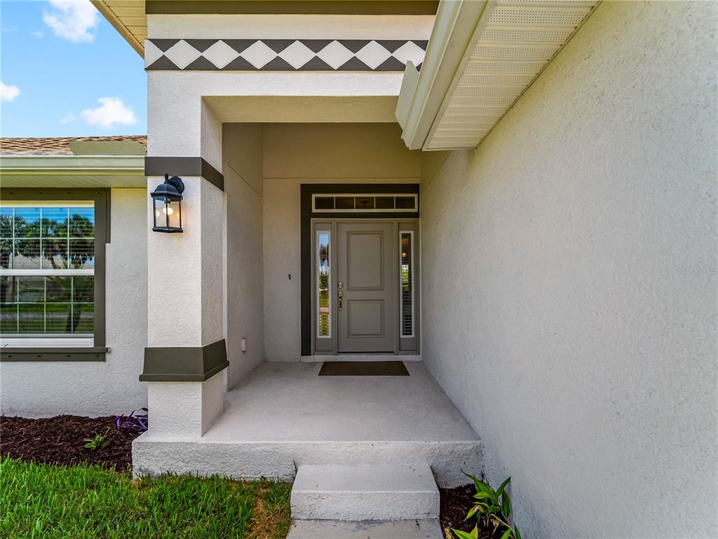 The front entrance features a gray door with sidelights under a covered porch — 55 PINE VALLEY LANE, ROTONDA WEST, FL