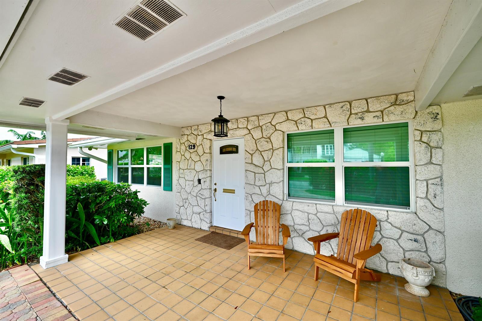 A covered porch features tan tile flooring, stone veneer walls, and two wooden Adirondack chairs — 129 Alhambra Place, West Palm Beach FL 33405, WEST PALM BEACH, FL
