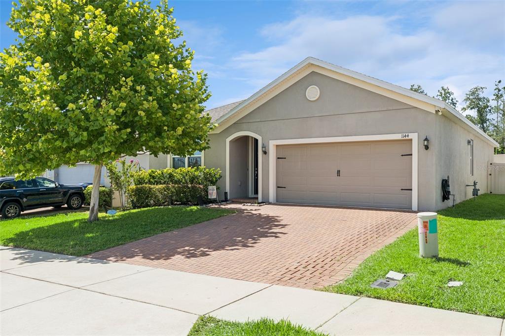 A single-story house with a beige stucco exterior, a brick driveway, and a two-car garage — 1144 CAVENDER CREEK ROAD, MINNEOLA, FL