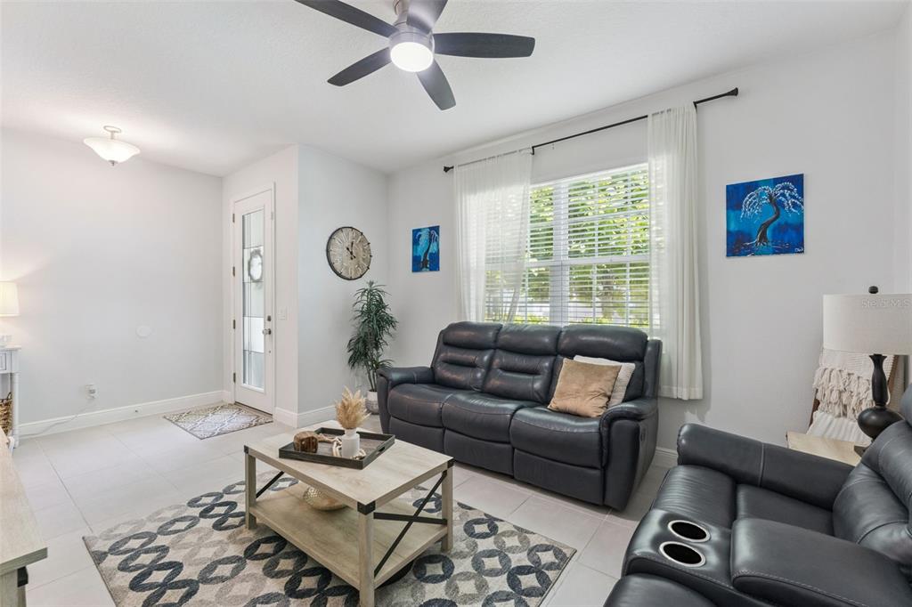 A living room features dark leather sofas, a patterned rug, and a ceiling fan — 1144 CAVENDER CREEK ROAD, MINNEOLA, FL