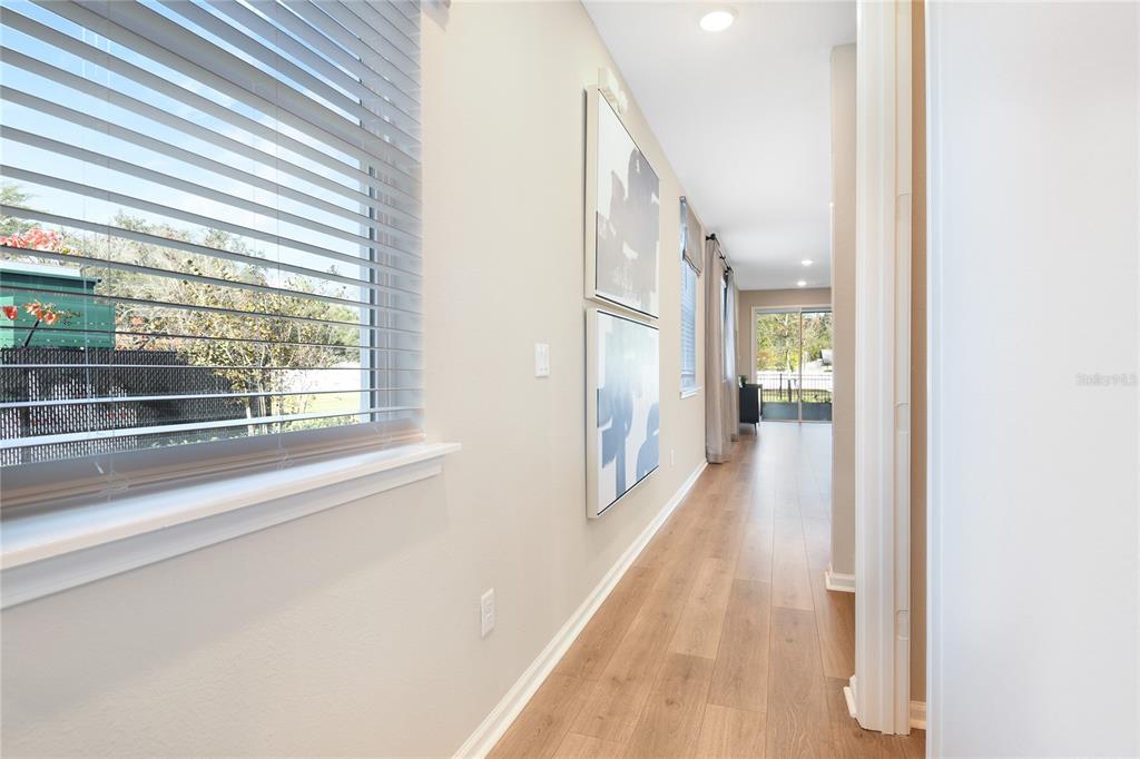 A hallway with wood-look flooring, two wall-mounted artworks, and a window with blinds — 2914 27TH AVENUE E, PALMETTO, FL