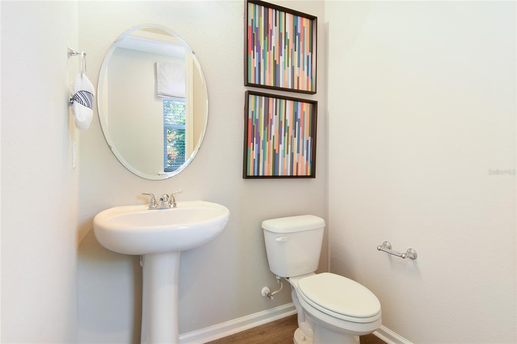 A bathroom features a pedestal sink, an oval mirror, a toilet, and two colorful wall art pieces — 2914 27TH AVENUE E, PALMETTO, FL