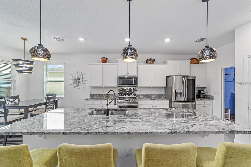 A kitchen features a large granite island, white cabinets, stainless steel appliances, and pendant lighting — 4395 NW 55TH TERRACE, OCALA, FL