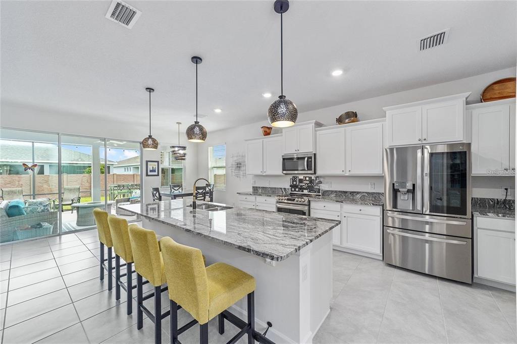 A kitchen features a granite island with yellow bar stools, white cabinetry, and stainless appliances — 4395 NW 55TH TERRACE, OCALA, FL