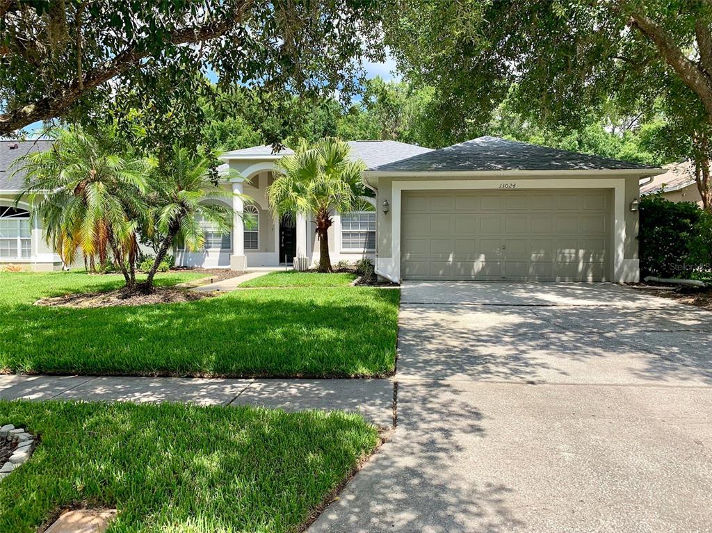 A single-story house features a two-car garage, a front lawn, and palm trees — 13024 ROYAL GEORGE AVENUE, ODESSA, FL