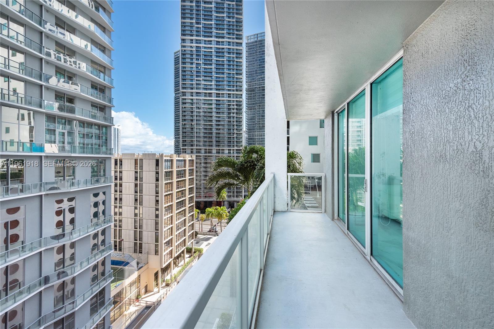 A balcony with a glass railing overlooks a dense urban area with several tall buildings — 55 SE 6 ST # 1207, Miami FL 33131, MIAMI, FL