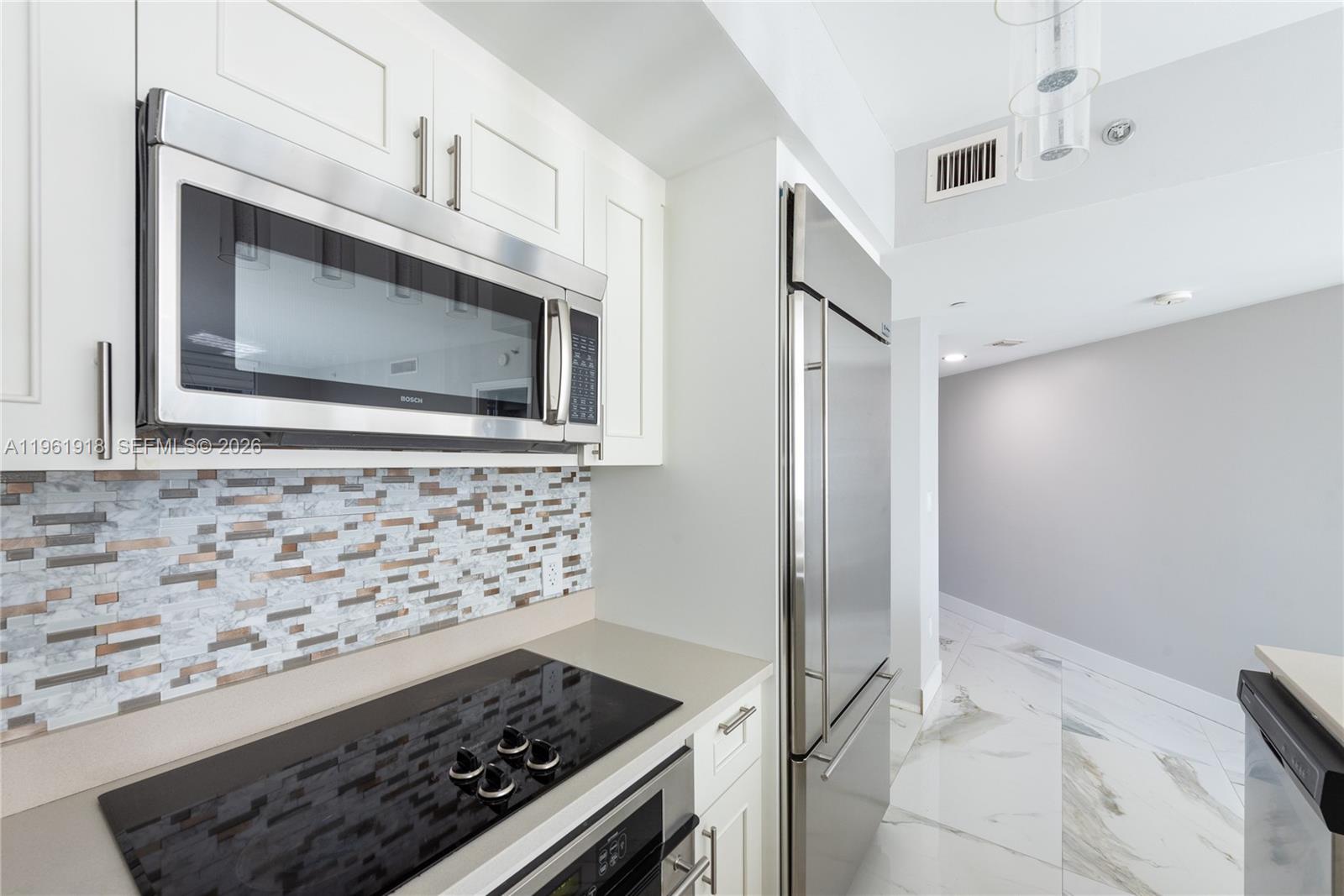 A modern kitchen features white cabinets, stainless steel appliances, and a marble-tiled backsplash — 55 SE 6 ST # 1207, Miami FL 33131, MIAMI, FL